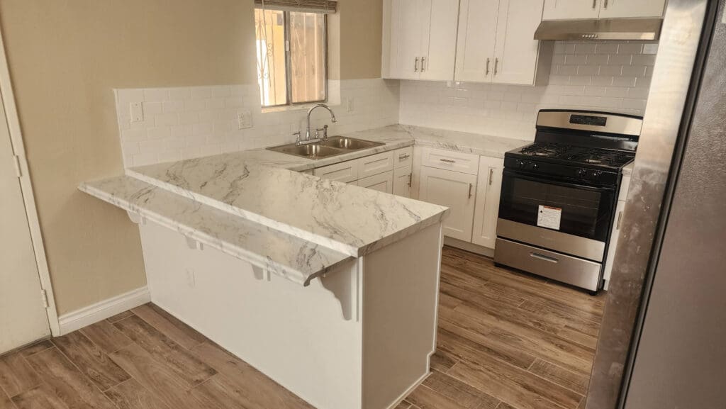 A kitchen with white cabinets and wood floors.
