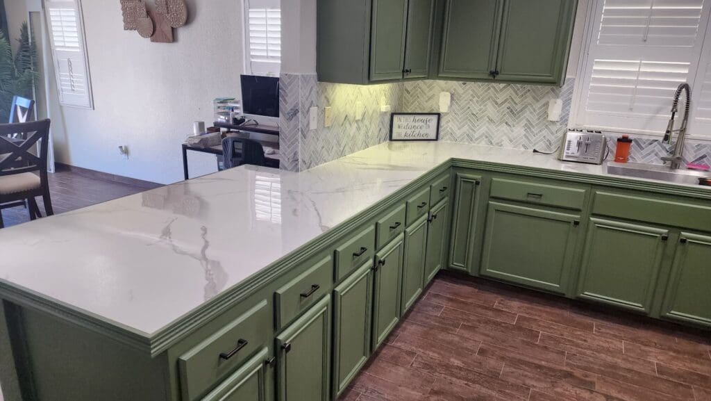 A kitchen with green cabinets and white countertops.